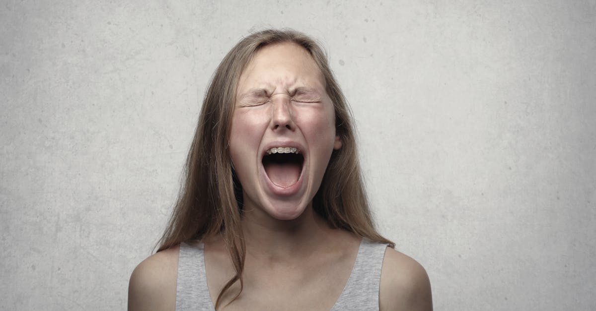 Young woman screaming with emotion, showing braces, against a gray backdrop.